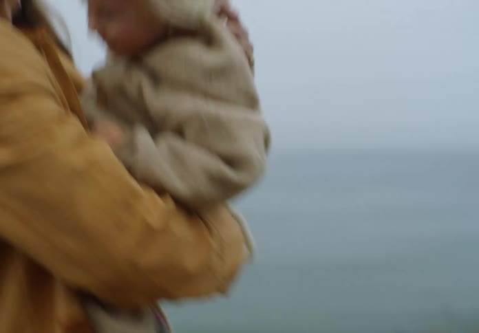Mother spins in place holding her daughter on the beach while they both laugh