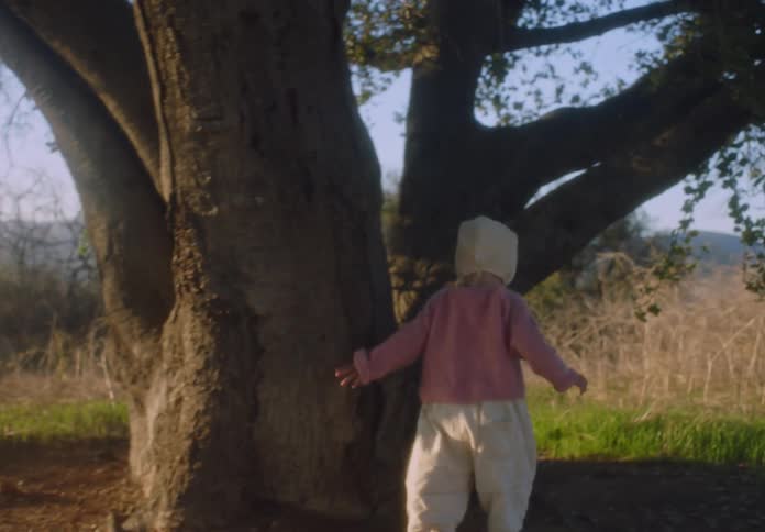 Mother plays with her daughter among a grove of large trees on a sunny autumn day