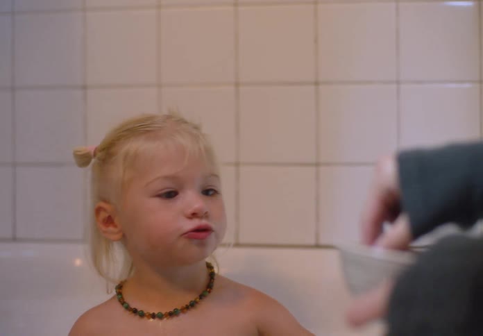 Mother drinks and feeds her daughter while the child sits in the bathtub