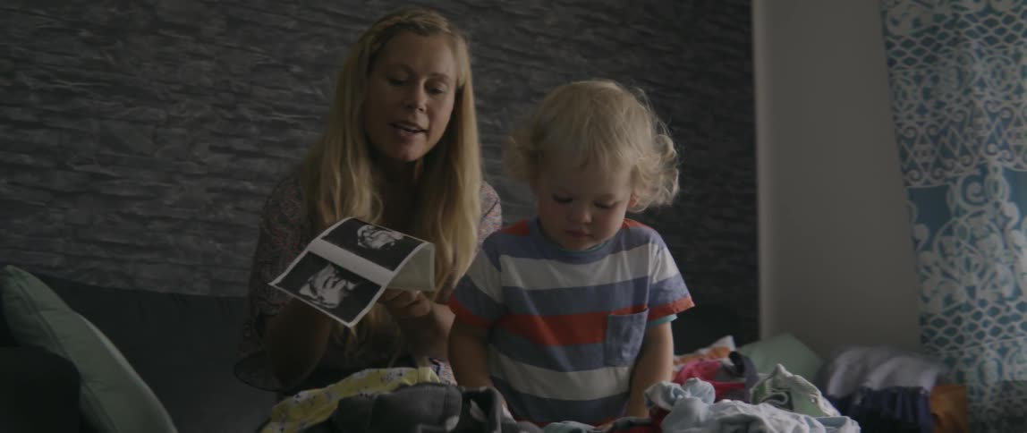 A woman talking to her toddler boy while looking at colorful pictures together indoors.