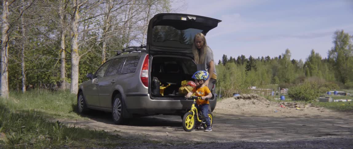 Mother unloading a child's bike from the back of a vehicle in the driveway.