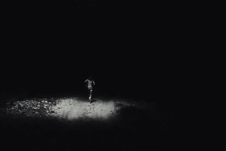 A person is jogging at night on a dirt path with a spotlight overhead