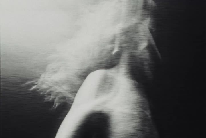 A blurry black and white view of a person running in place on a platform in a dark space with a single bright light from above creating high contrast and a sense of fast motion