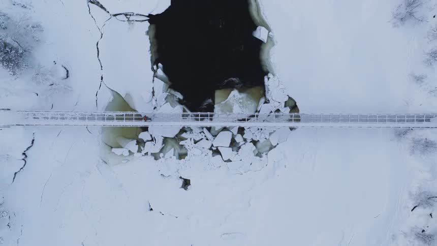 The man crosses the small bridge over the ice