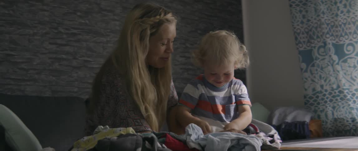 Woman talking to toddler boy as he plays with baby clothes in living room