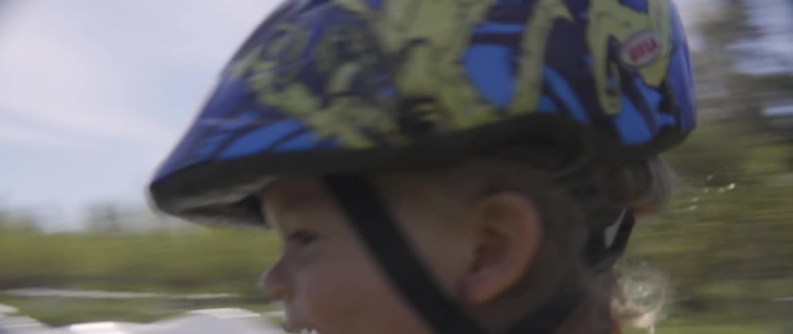 A young boy rides a balance bike with a woman walking behind