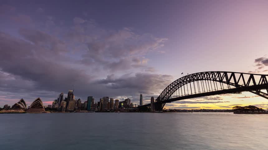 Boats sail along the coast by the sydney opera house and downtown buildings