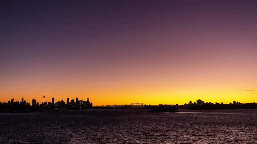 A timelapse captures the transition from a fiery orange sunset to a deep purple twilight over the sydney skyline and harbour bridgedark clouds gradually clear away to reveal a clear night sky as city lights begin to twinkle across the hori