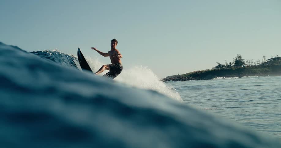 Surfers riding and catching a rising wave in the open ocean under a clear sky