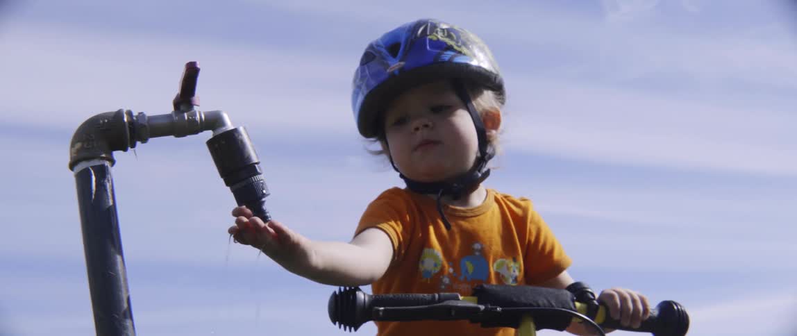 A boy on a bicycle holds his hand under a dripping water faucet