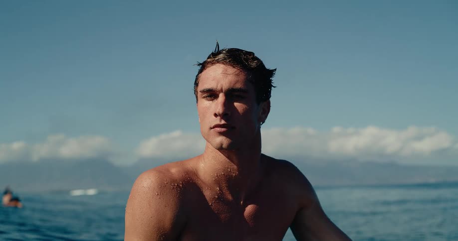A man sits in the ocean on a surfboard with his head above the water while looking toward the horizon