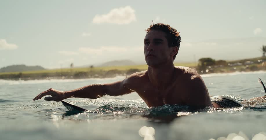 Man lying on a surfboard paddling in water off the coast among other people