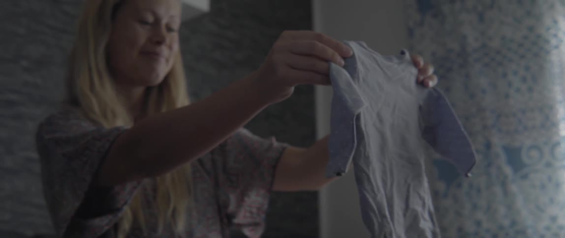 Woman holding a child's piece of clothing in front of her and smiling