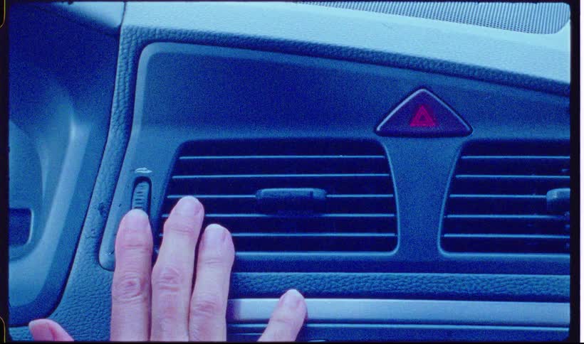 A hand adjusts the air conditioning vent in the dashboard of a car