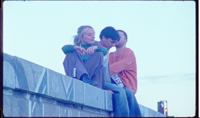 A group of three young adult friends sit on a concrete wall at a marina