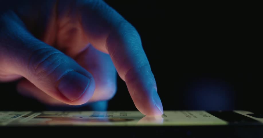 A finger scrolls through content on a smartphone screen in a dark environment