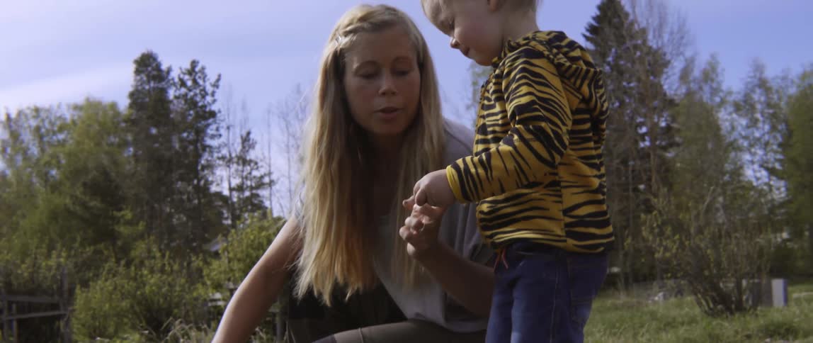 Woman giving a berry to her toddler in a field on a cloudy day