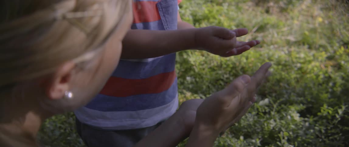 Young woman offering handful of ripe berries to a boy during a summer outing.