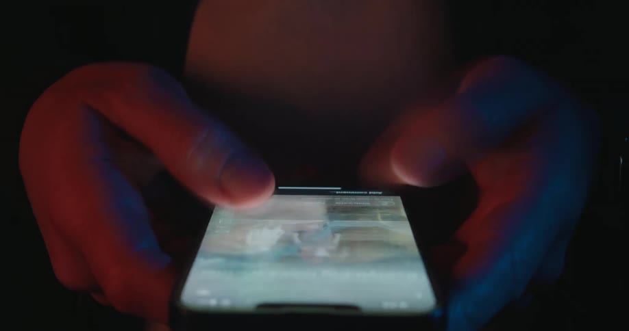 A person using both thumbs to scroll rapidly through a social media feed on a smartphone the dark environment is illuminated primarily by the glow of the screen highlighting the fastpaced nature of digital content consumption