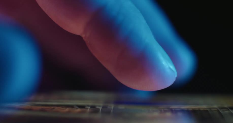 A close view from the side shows a finger scrolling through various colorful images on a mobile phone screen in a dark room with blue light
