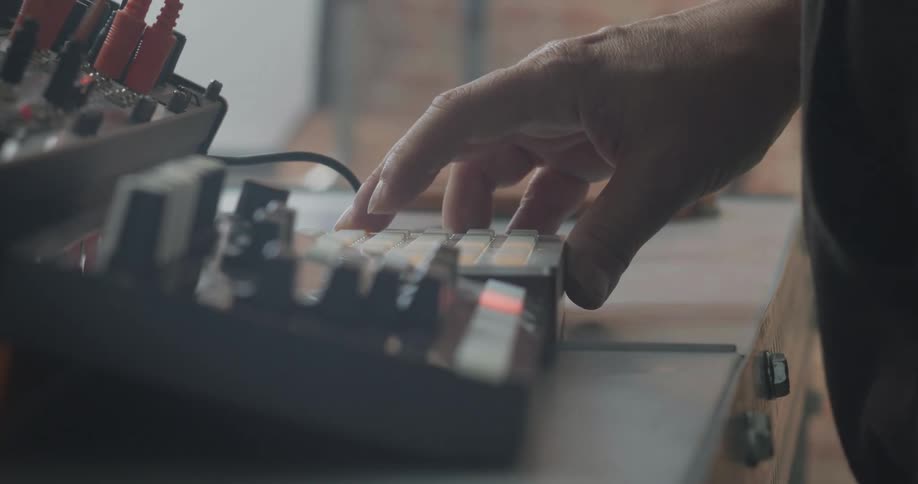 A persons hand is hitting buttons on a machine with buttons and wires in a room