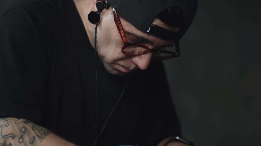 A man wearing glasses and a baseball cap focuses on performing a task with his hands