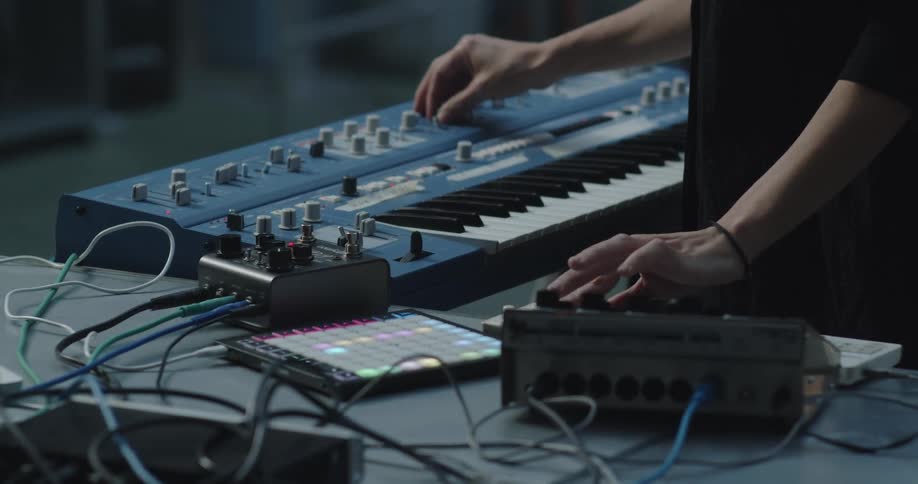 Person adjusting a synthesizer and electronic music controller on a table