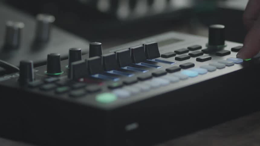 A person presses buttons and adjusts a slide on an audio mixing console