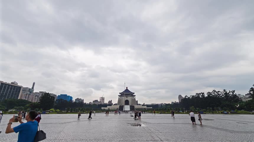 Large plaza with traditional pavilions and a central monument under a cloudy sky