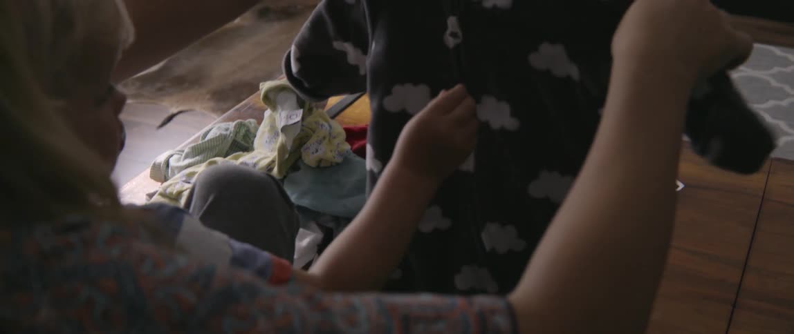 Toddler boy looking at his pajamas with his mother in living room