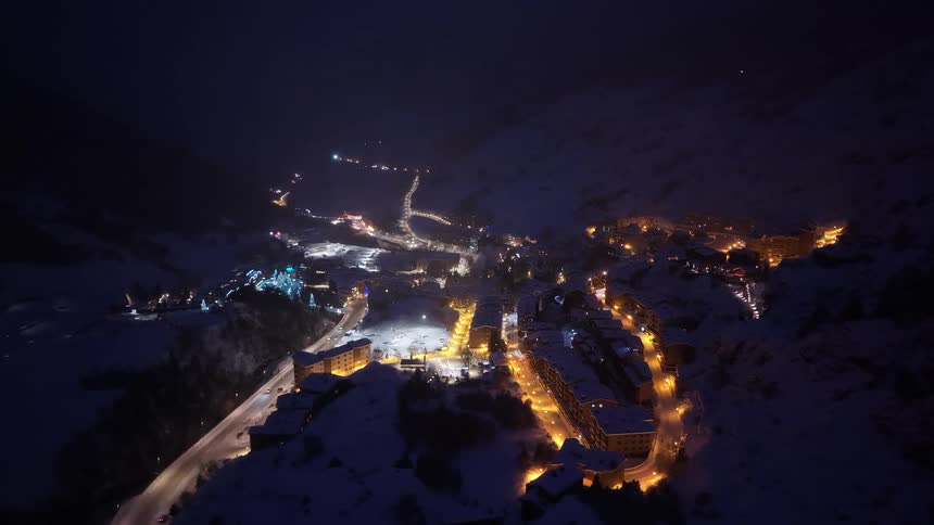 An aerial view shows a snow covered mountain village illuminated by street lights at night