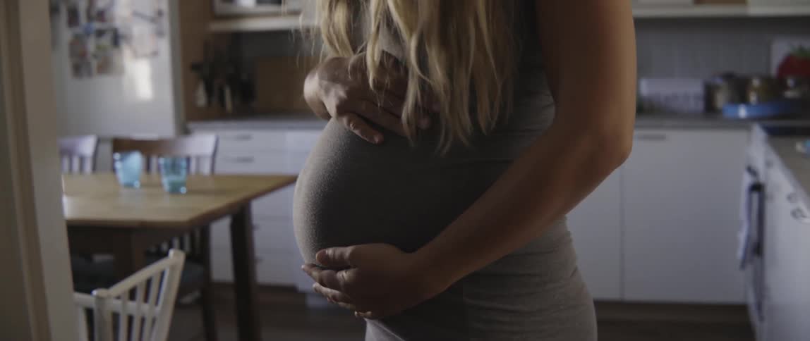 Candid moment of a pregnant woman smiling and touching her belly during the day.