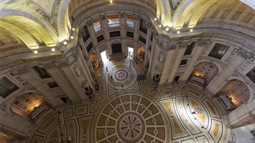 Symmetrical marble floor and soaring arched walls of a grand cathedral rotunda where golden light illuminates the intricate stone patterns and religious architecture of the historic interior space