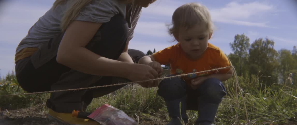 A woman stops a child from eating a seed they are planting in a garden