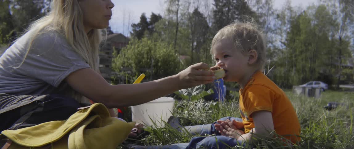 Mother and toddler boy sharing a snack together while sitting in a garden.