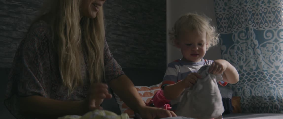 Mother and young child folding laundry together while sitting in a natural home setting.
