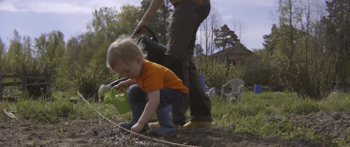 Mother and son using a watering can to care for plants in nature.