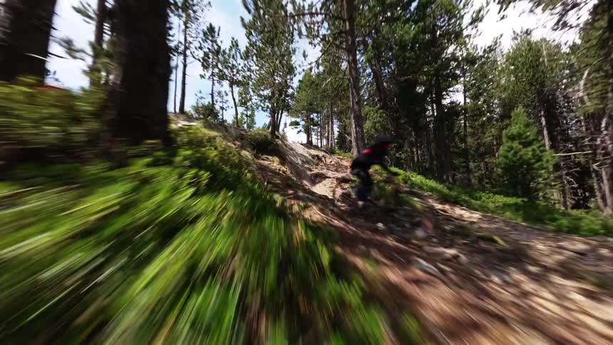 Cyclist rides a bike on a forested mountain trail under a cloudy sky