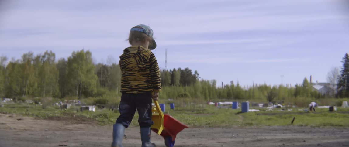 Authentic lifestyle footage of a toddler pushing a red toy wheelbarrow outdoors.
