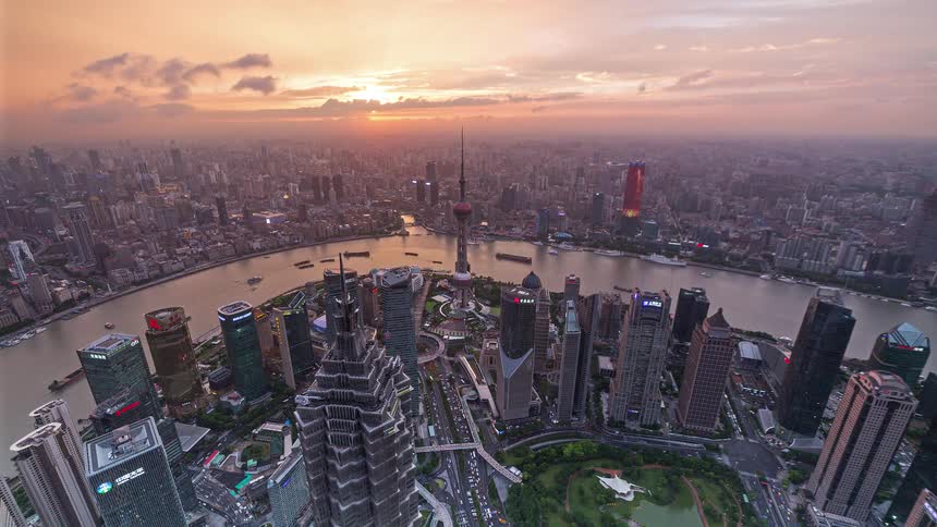 A panoramic timelapse captures the transition from daylight to a vibrant neon night over the shanghai skyline the sun sets behind the citys dense skyscrapers casting a deep orange glow that gradually fades into purple and blue