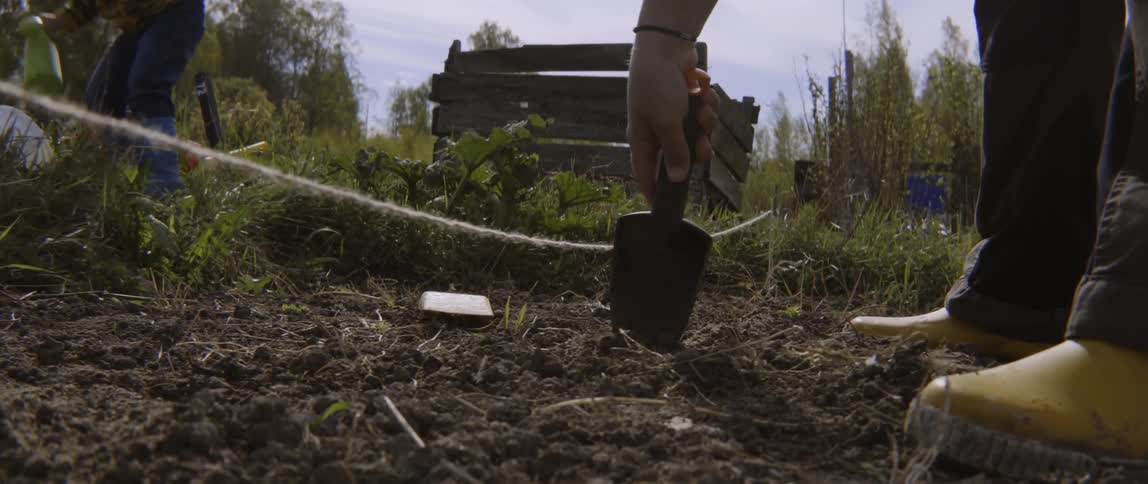 Woman digging in garden soil while toddler boy plays nearby