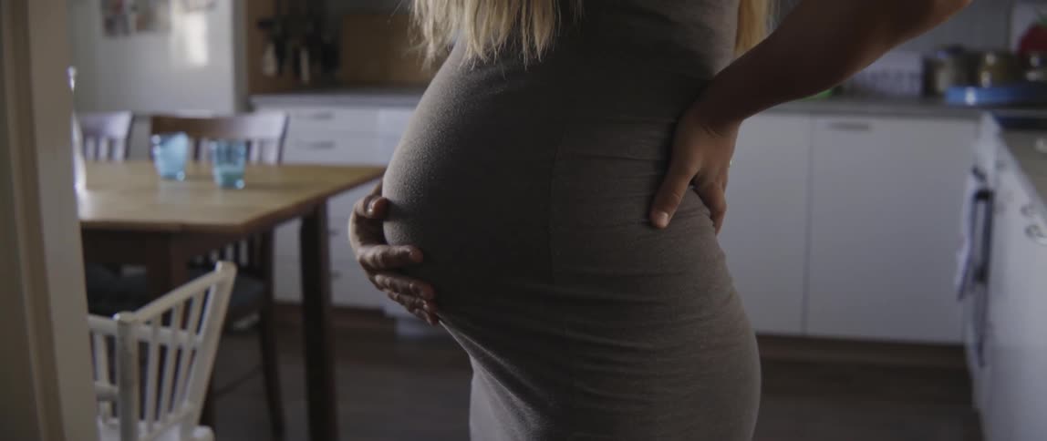 Pregnant woman standing in a modern kitchen while preparing a healthy meal at home.