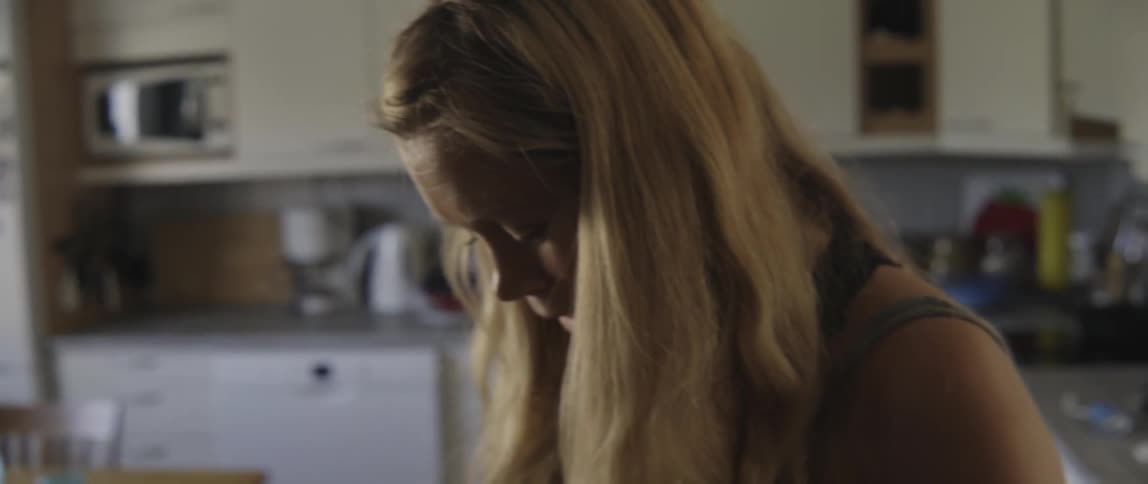 A woman stands in a kitchen and rubs her pregnant belly