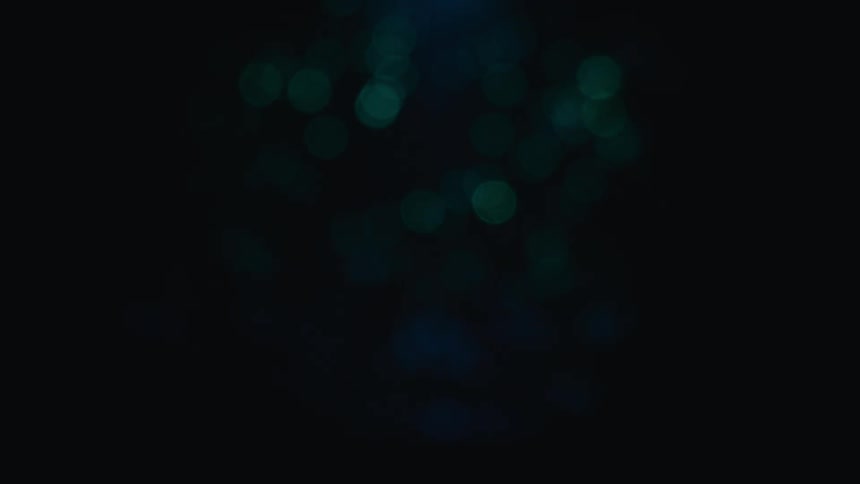 Soft blurry circles of green light drift slowly against a dark black background creating a gentle bokeh effect