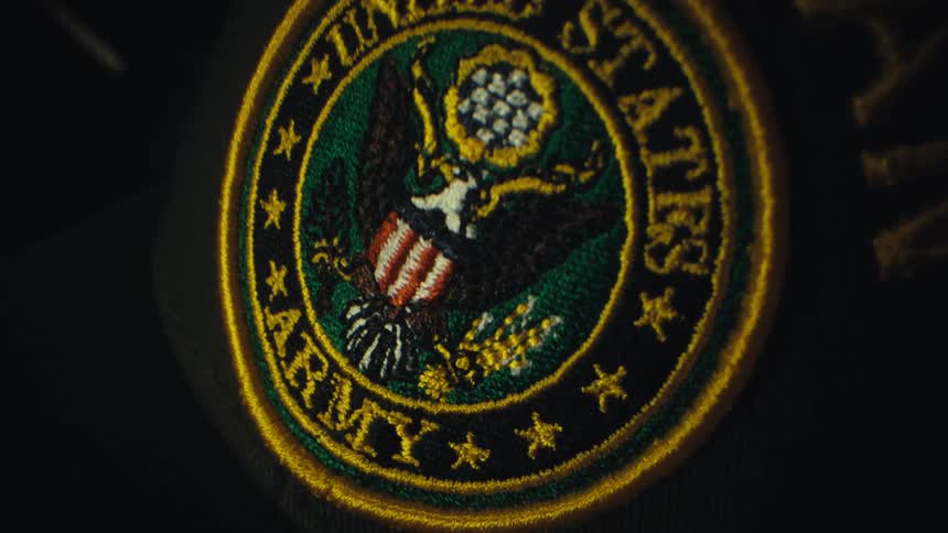 A close up shot of an embroidered united states army veteran patch sewn onto a black hat featuring a detailed eagle emblem surrounded by gold stars and text in a dark environment with soft lighting