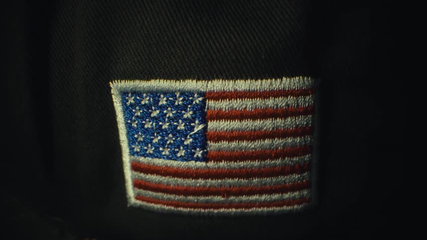 An embroidered american flag patch with white stars and red stripes is sewn on a green fabric