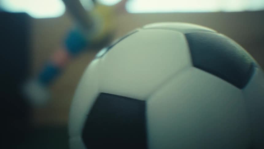 A close view shows a black and white soccer ball and the plastic players on a table soccer game