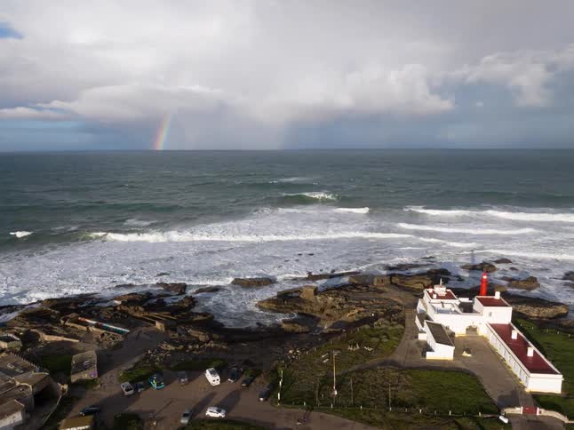 White lighthouse by the sea with strong waves and a rainbow on the horizon