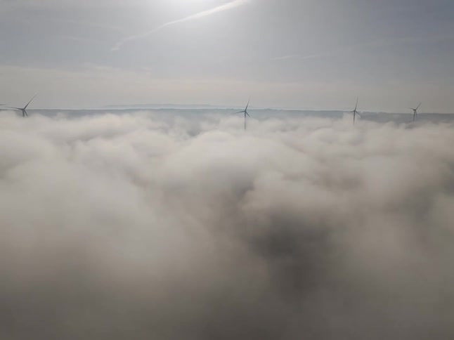 Aerial view of a sea of clouds with wind turbines in the background
