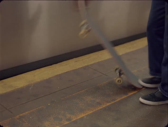 Person placing one foot on a skateboard on a subway station platform